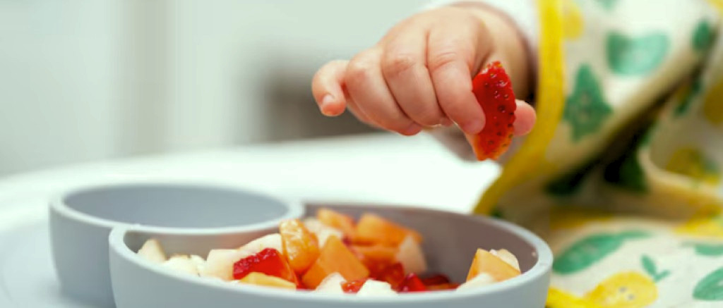 Bébé qui goûte un nouvel aliment, une fraise.