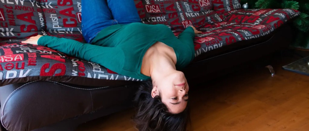 Femme positionnée la tête en bas sur un canapé.